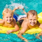 Young Kids Having Fun in Swimming Pool on Yellow Raft. Summer Vacation Fun.